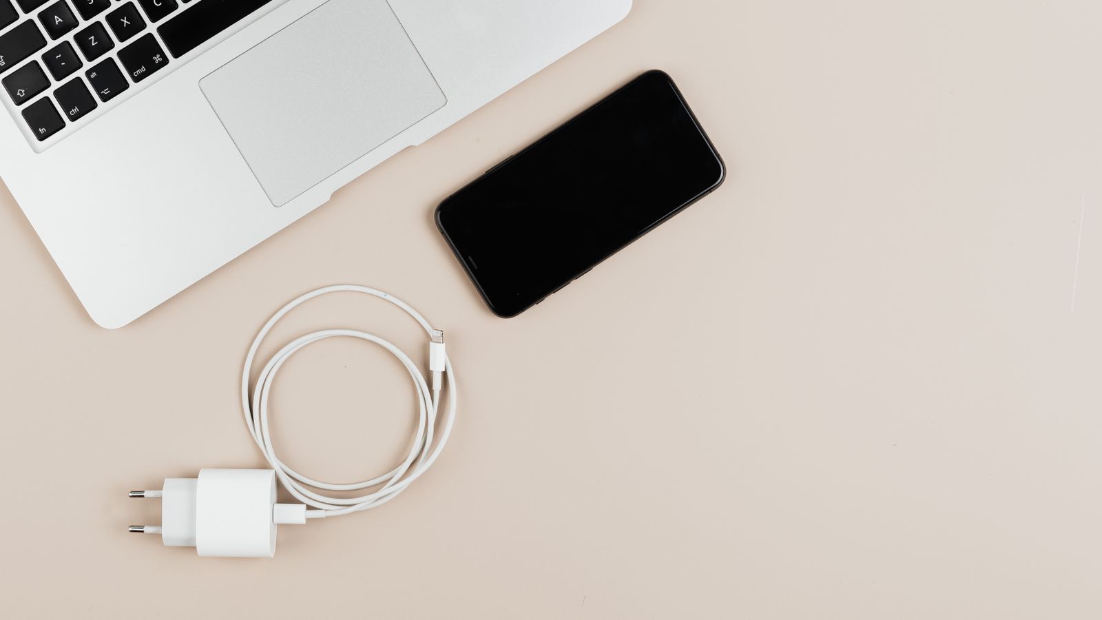 Laptop, smartphone, charger, and cable arranged on a neutral desk